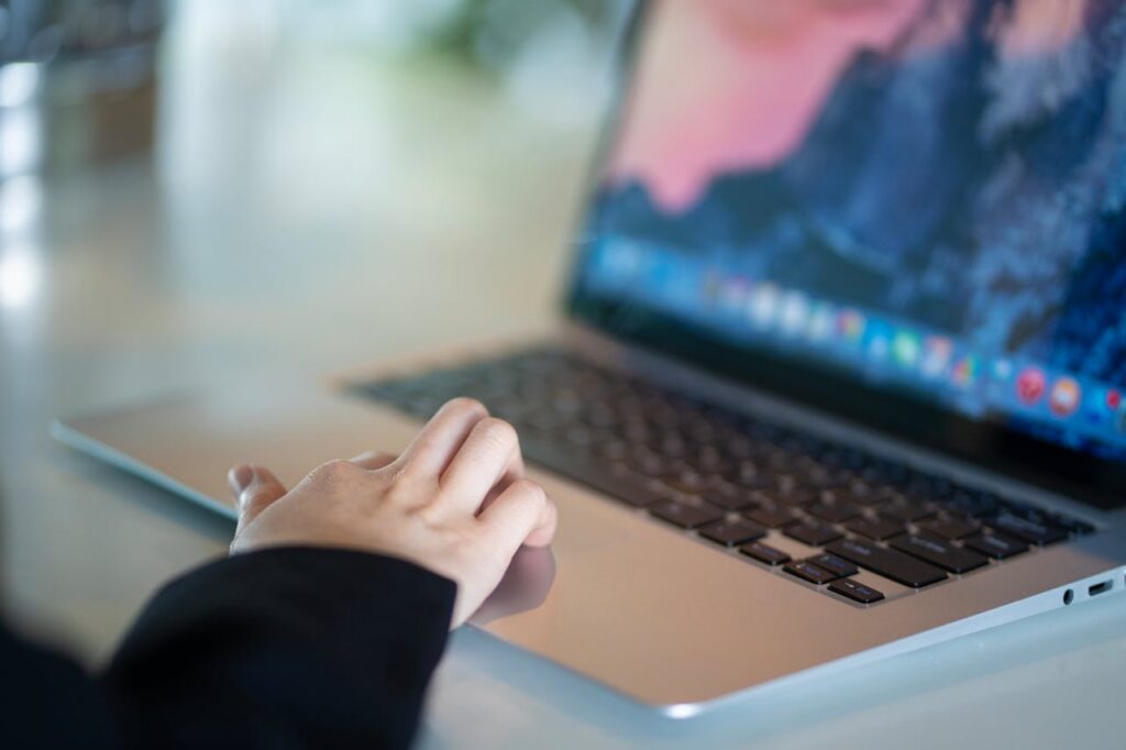 Close-up of a hand using a laptop in a modern office environment, symbolizing remote work.