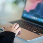 Close-up of a hand using a laptop in a modern office environment, symbolizing remote work.